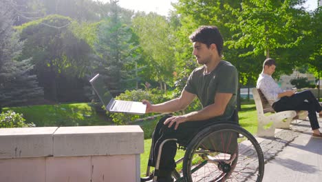 Teenager-sitting-in-wheelchair-working-with-laptop-outdoors.